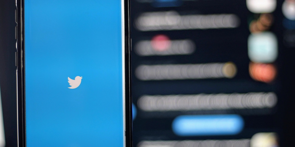 An image of a phone with the Twitter Logo in front of an abstract background